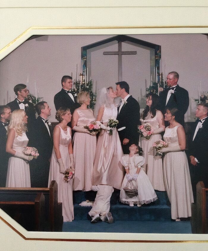 Bride and groom kissing at church wedding surrounded by bridal party in an awkward wedding photo with a person bent under the bride.