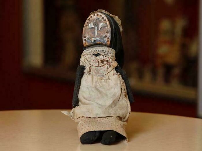 Worn Victorian era doll with fabric dress and painted face sitting on a table, showcasing vintage 19th century style.