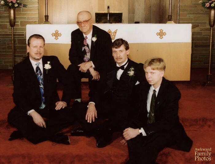 Four men in tuxedos posing awkwardly on the floor in a church, a classic example of awkward wedding photos.