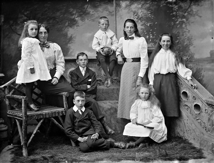 Victorian era family portrait featuring children and adults in period clothing posing outdoors on stairs.