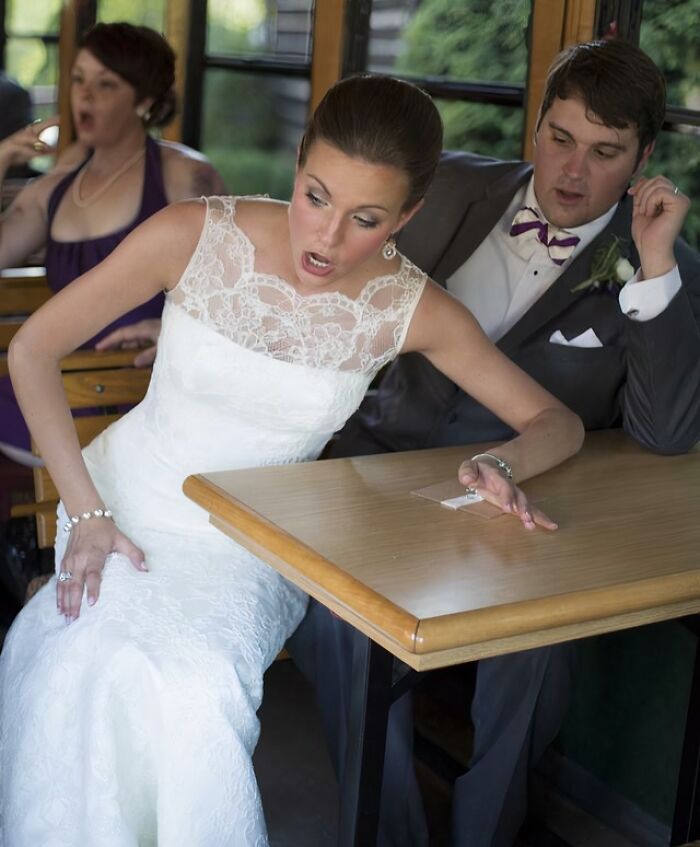 Bride and groom in awkward wedding photo reacting with surprise while sitting at a wooden table inside a vehicle.