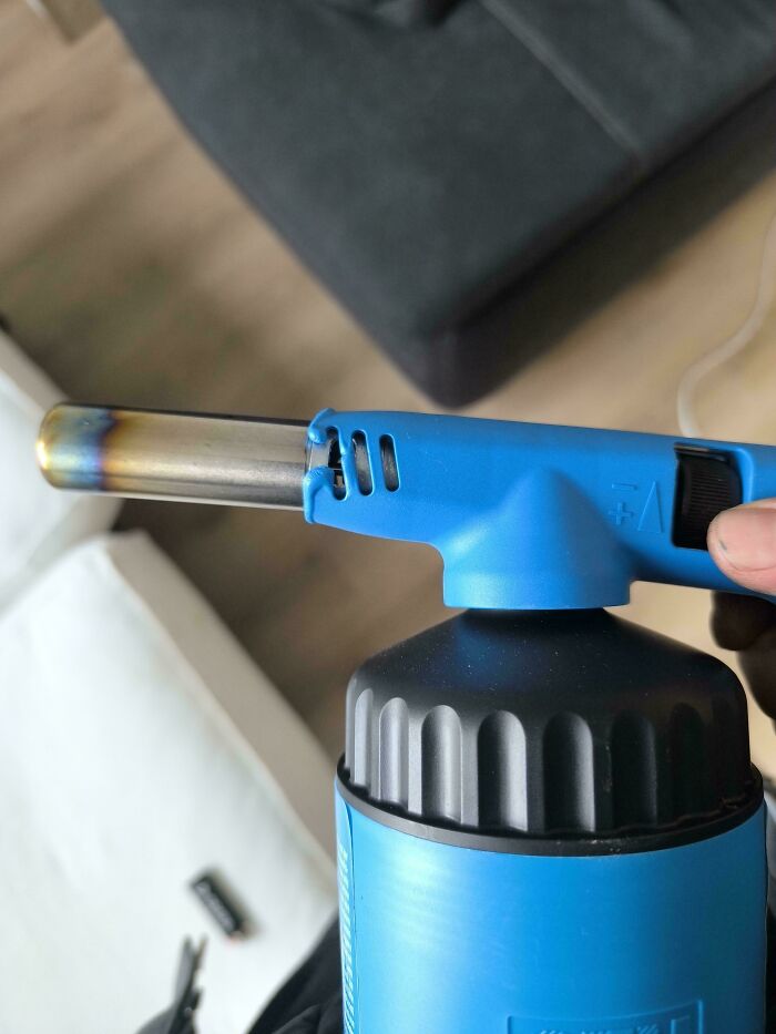 Blue butane torch with a metal nozzle held indoors, illustrating terrible product designs that make no sense.