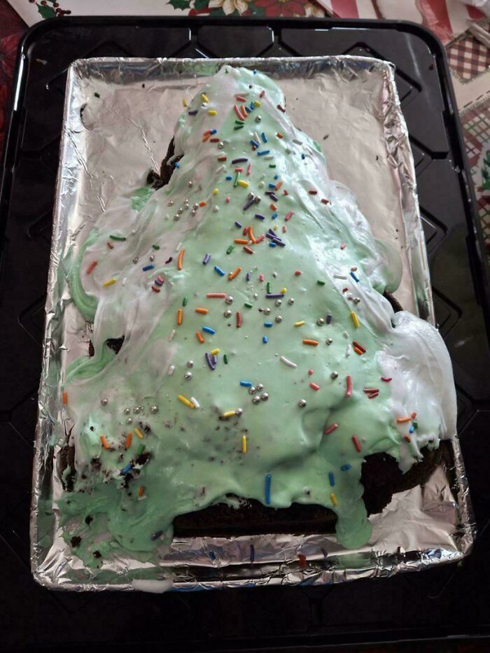 Green frosted cake shaped like a Christmas tree with uneven icing and colorful sprinkles, a dessert ruin fail.