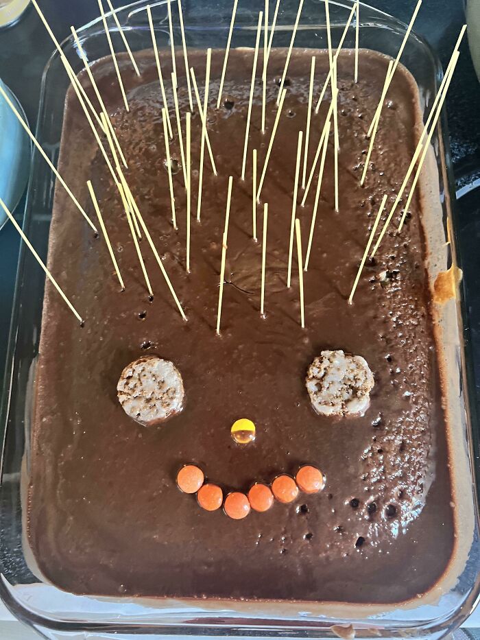 Baking disaster with a burnt chocolate dessert decorated awkwardly with cookies, candy, and uncooked spaghetti sticks.