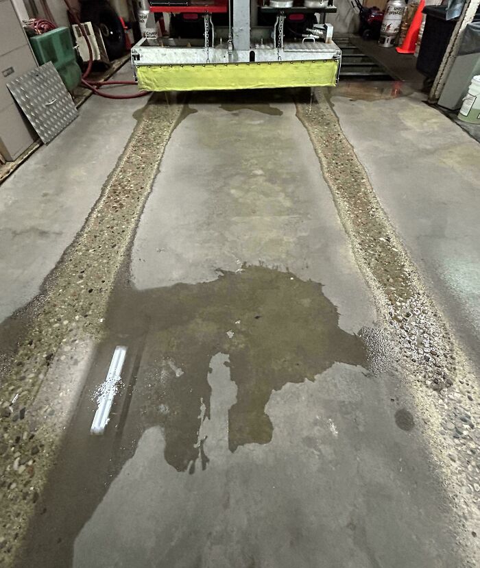 Concrete floor worn down in unexpected ways by heavy machinery creating exposed aggregate tracks in a workshop.