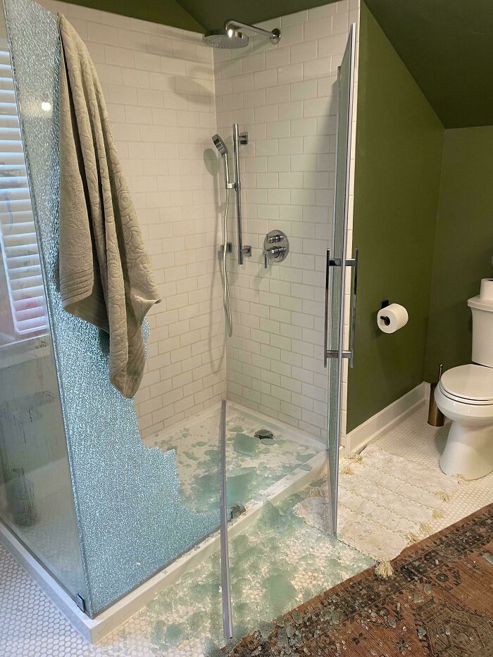 Broken glass shower door with shattered fragments inside bathroom, a costly and unfortunate fail in home renovation.