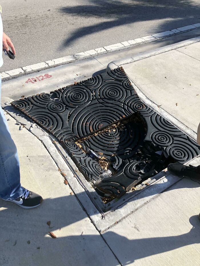 Sidewalk manhole cover with a large hole in the center, illustrating an unfortunate and expensive fail involving public infrastructure.
