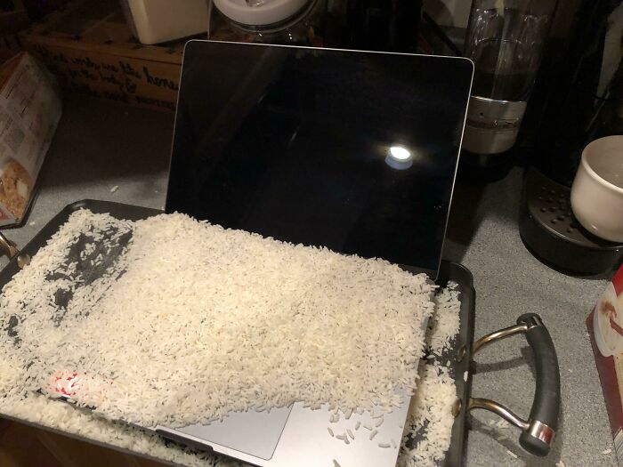 Laptop covered in uncooked rice on a kitchen counter illustrating an expensive and unfortunate fail.
