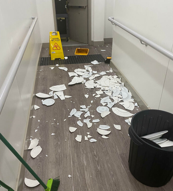 Broken white plates scattered on a hallway floor with caution sign and broom, showing an unfortunate and expensive fail.