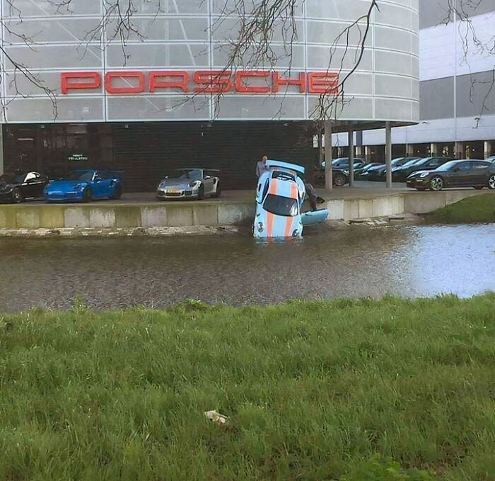 Porsche car partially submerged in water near dealership, showcasing an unfortunate and expensive fail outside the showroom.