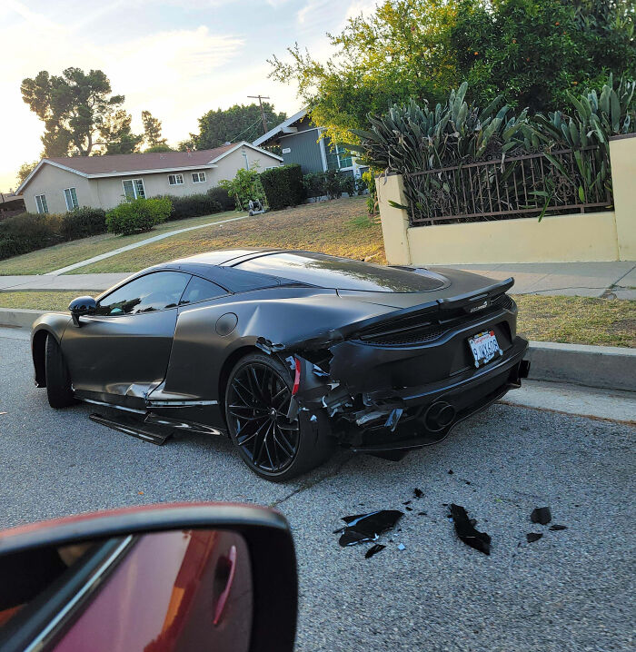 Black sports car with extensive rear damage parked on a residential street, showing an expensive and unfortunate fail.