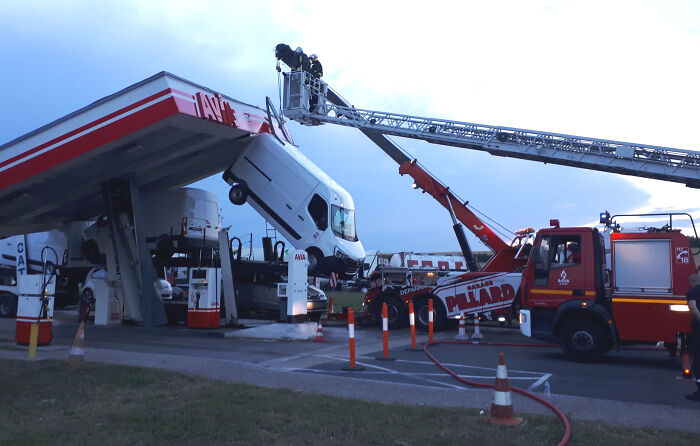 White truck crashed into gas station roof with emergency responders using a crane to remove it in expensive fail scene.