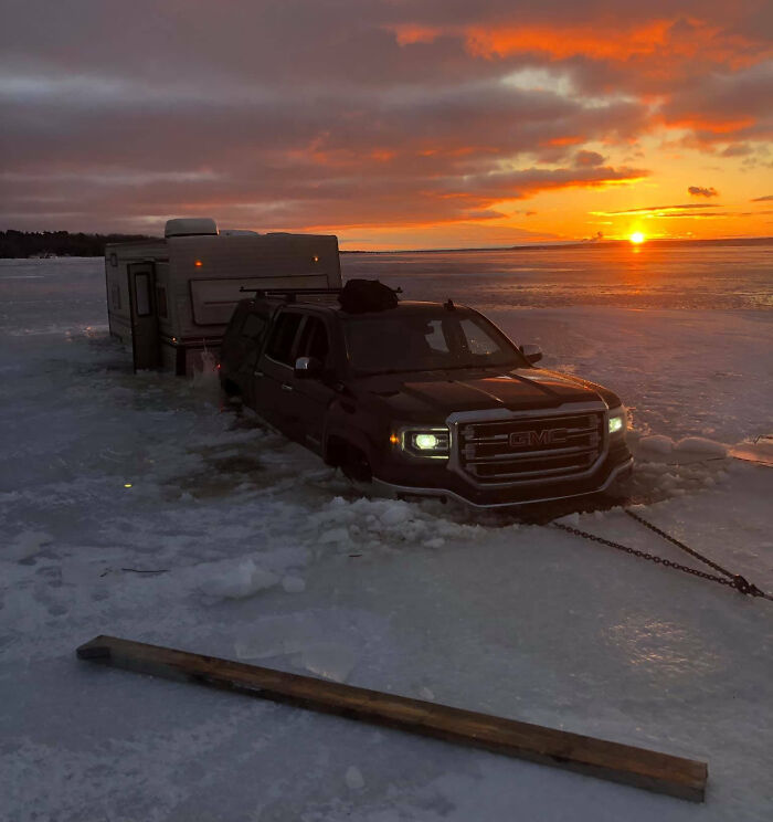 Black GMC truck and trailer stuck in frozen lake ice at sunset, showcasing expensive unfortunate and stupid fails.