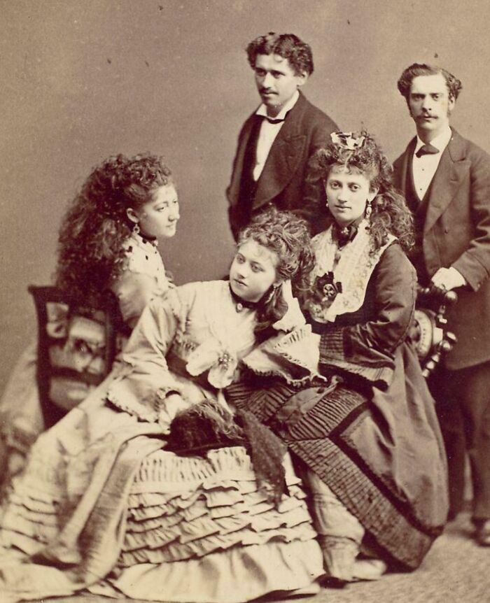 Group of Victorian era people dressed in period clothing posing for a formal vintage photograph.