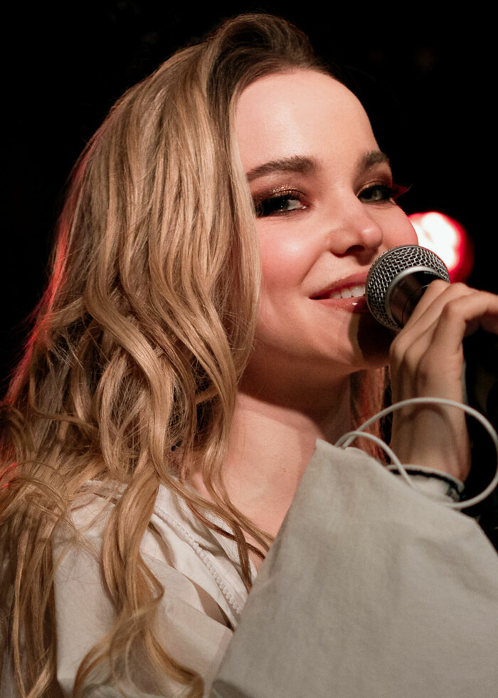 Dove Cameron performing on stage with microphone, showcasing her bio and career highlights in entertainment.