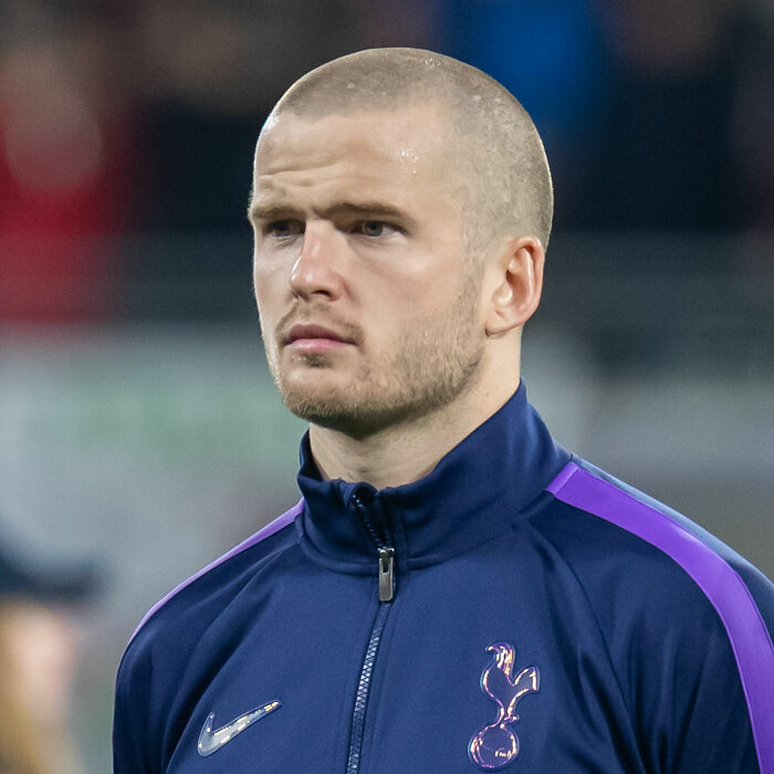 Eric Dier in a navy and purple Tottenham Hotspur jacket, focused and ready during a football match.