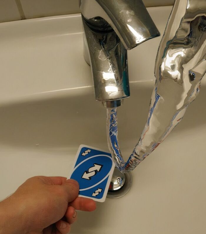 Hand holding an Uno reverse card under a faucet with water shaped like a large reverse arrow in a confusing funny picture.