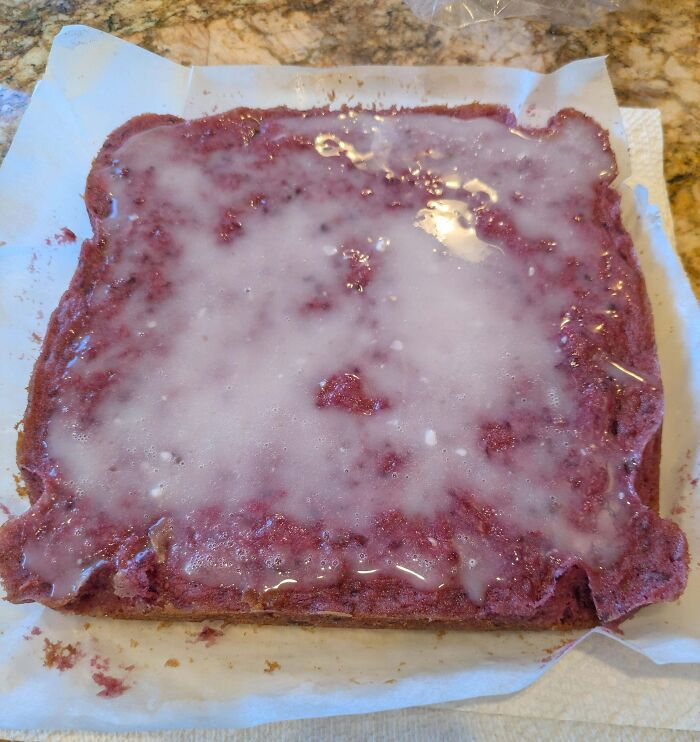 Failed red velvet cake with uneven glaze spread on parchment paper, an example of ruined dessert attempts.