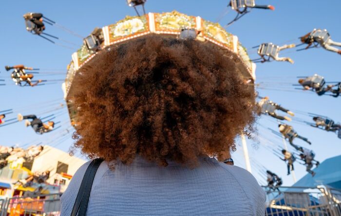 Person with curly hair viewed from behind watching a colorful swing ride, a street photo capturing unexpected and beautiful moments.