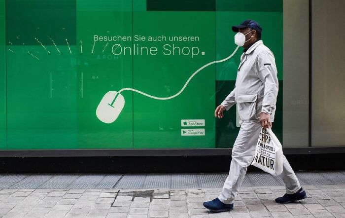 Man wearing a mask walking past green storefront with online shop advertisement in a candid street photo capturing unexpected moments