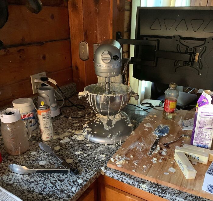 Kitchen counter with a stand mixer overflowing with batter, surrounded by a messy spill of ingredients and utensils, showing dessert ruin.