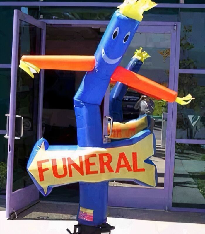Inflatable dancing tube man holding a funny funeral sign outside a building in a confusing picture.