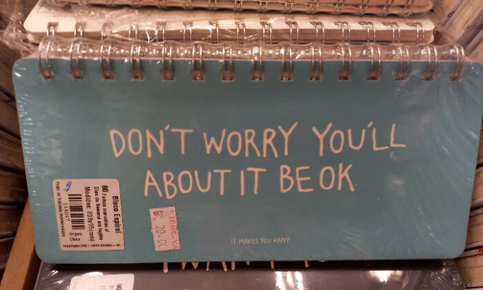 Blue spiral notebook with a humorous design fail where the text says "DON'T WORRY YOU'LL ABOUT IT BE OK" showing design writing mistakes.