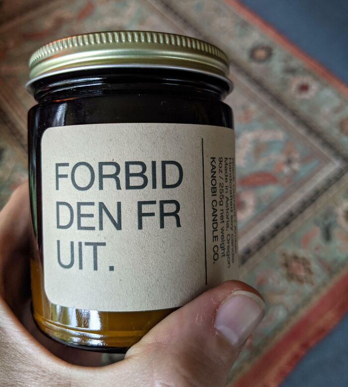 Hand holding a candle jar with a label showing a design fail in text spacing and layout by designers.