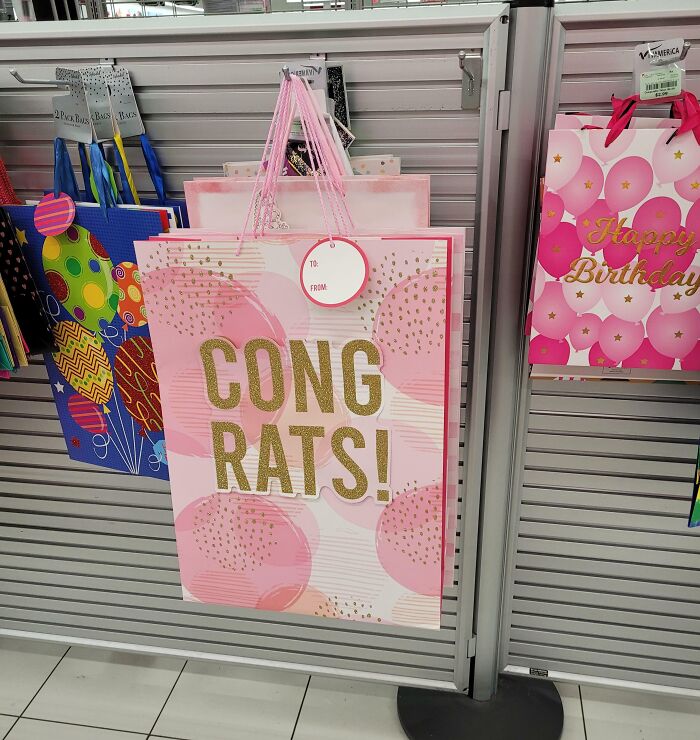 Gift bags with designer writing fail showing "CONG RATS!" message in a store display with other colorful bags.