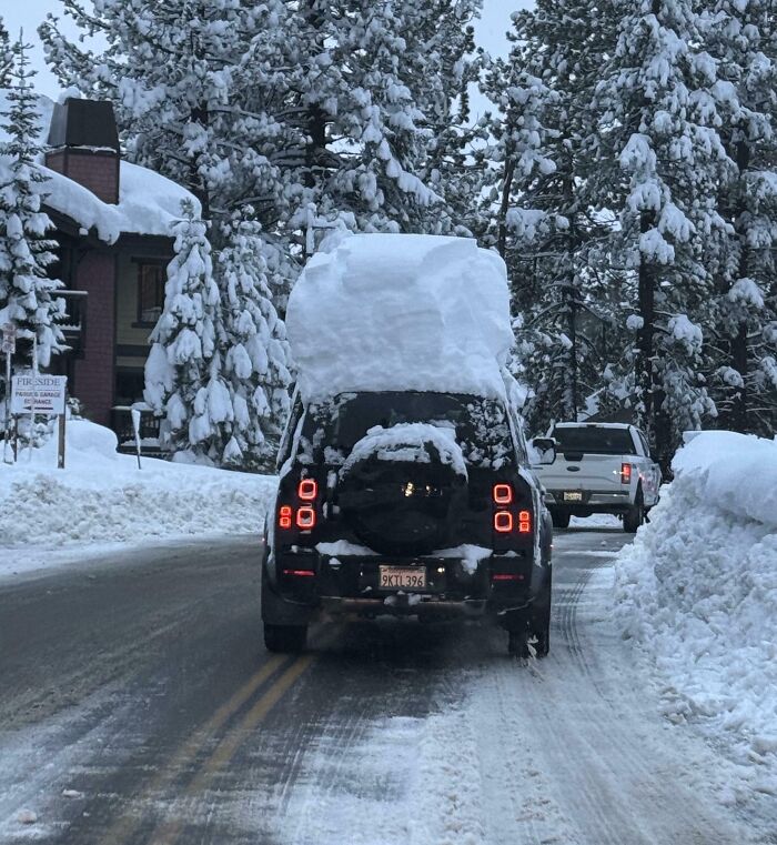 SUV driving on snowy road with large snow pile on roof, illustrating reckless and dumb drivers on winter streets.