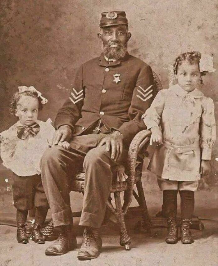 African American Civil War veteran in uniform seated with two young children in a historic US history photo.