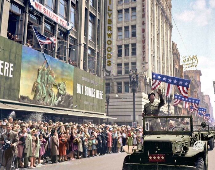 Crowd celebrating with American flags and soldier in military jeep during a historic US history moment on city street.