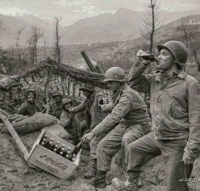 US history photo of soldiers in a trench sharing Coca-Cola bottles during World War II, showing a unique moment from the past.