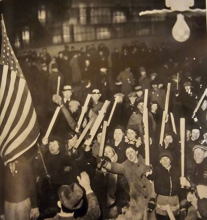 Crowd of people holding wooden bats and an American flag in a historic US history photo showing unrest in the past.