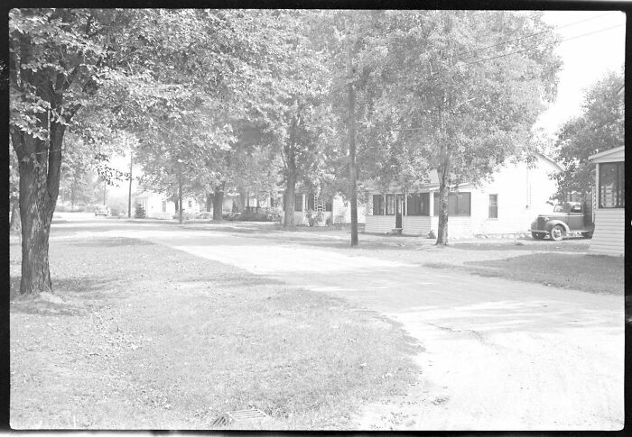 Quiet US history photo of a tree-lined rural street with classic houses and a vintage car parked by the road.