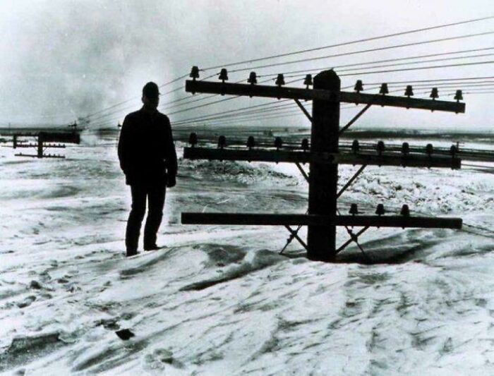 Silhouette of a man standing near telephone poles buried in deep snow during a historic US winter storm.