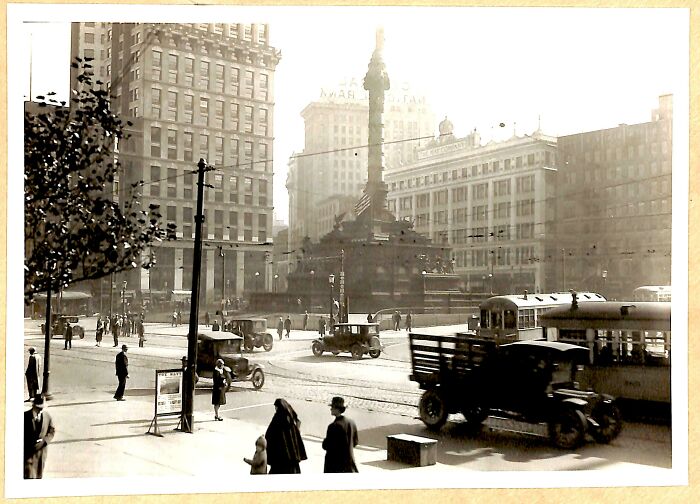 Vintage black and white photo showing early 20th century city traffic and pedestrians, a US history scene beyond textbooks.