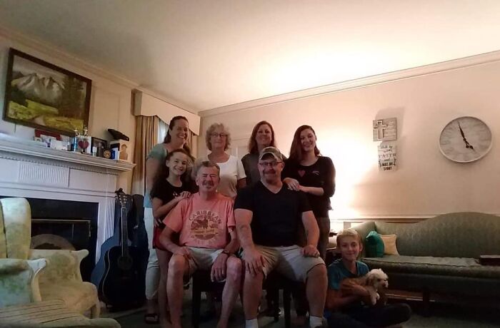 Group of family members sitting and standing in a living room, sharing a moment connected to a late son's heartbeat teddy bear.
