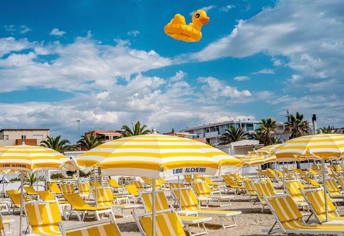 Beach scene with yellow umbrellas and a floating rubber duck, capturing street photos by Perry Hall's style.