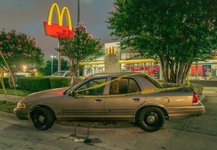A street photo capturing a taped-off car parked near a McDonald's at night, showing life exactly as it happens.