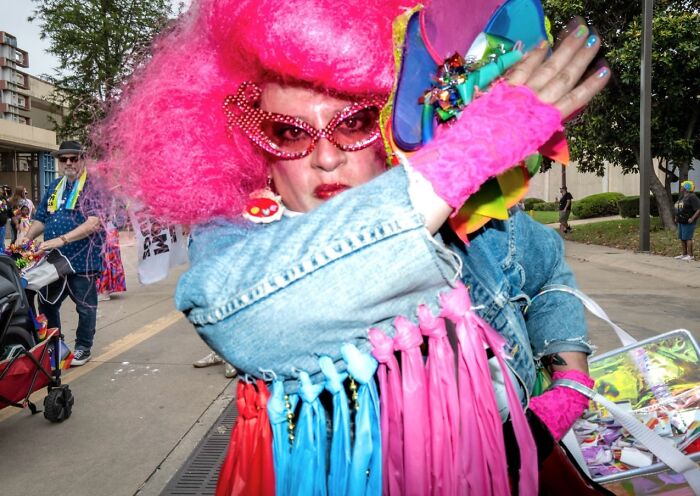 Colorful street photo showing a person in bright pink wig and glasses at a lively outdoor event capturing life exactly as it happens.