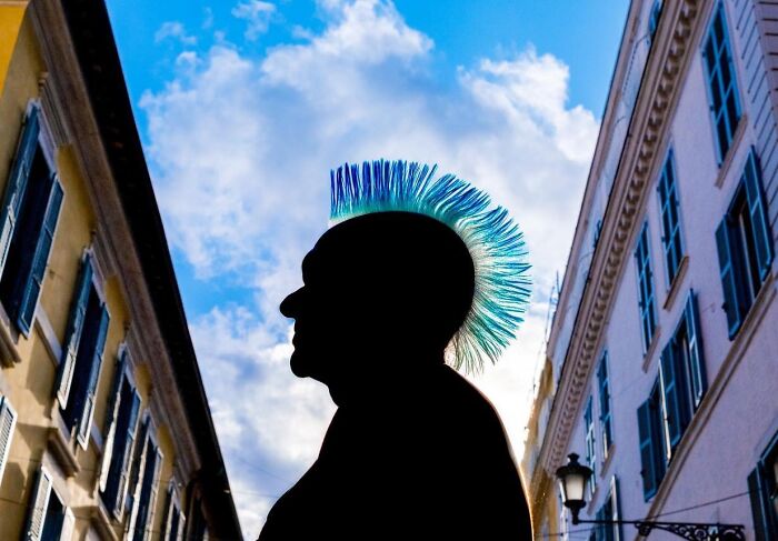 Silhouette of person with colorful mohawk hairstyle against a blue sky in a street photo by Perry Hall.