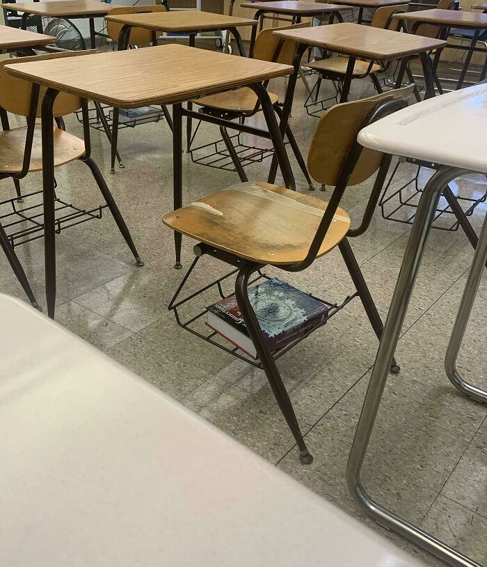 Empty classroom with old wooden desks and a textbook shoved under one chair showing weird teacher behavior in class.
