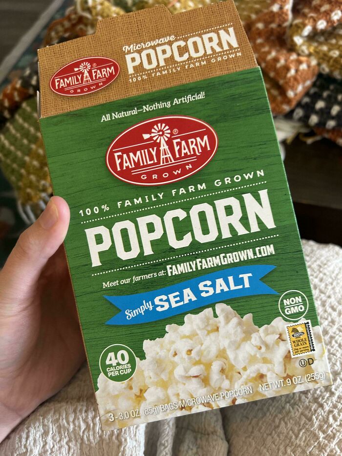 Popcorn box held in hand with sea salt flavor, highlighting natural ingredients and family farm grown branding.