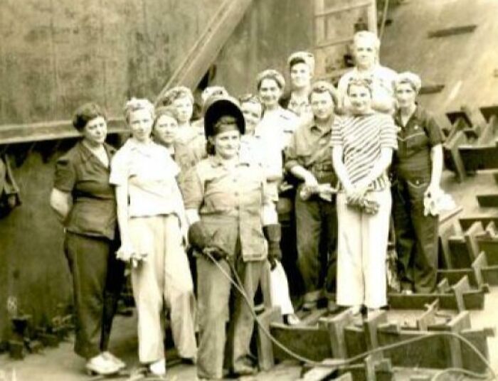 Group of women factory workers in vintage clothing posing together in a historical US history photo from the past.