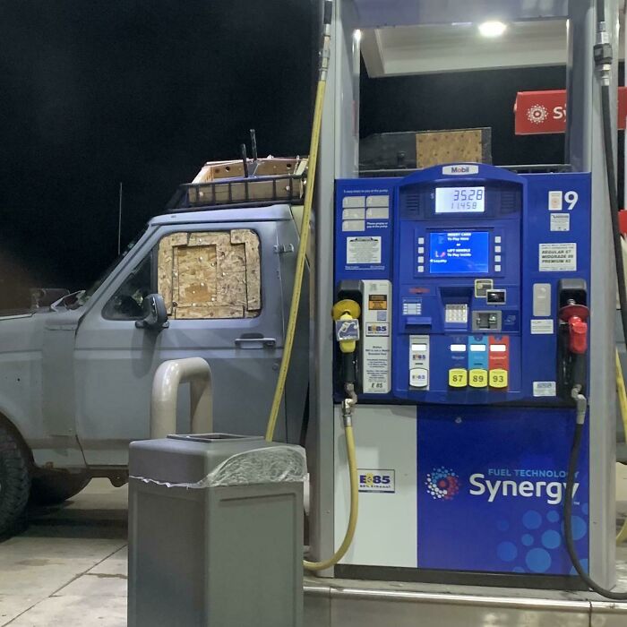 Old SUV with windows boarded up fueling at a gas station, an example of dumb drivers being shamed.