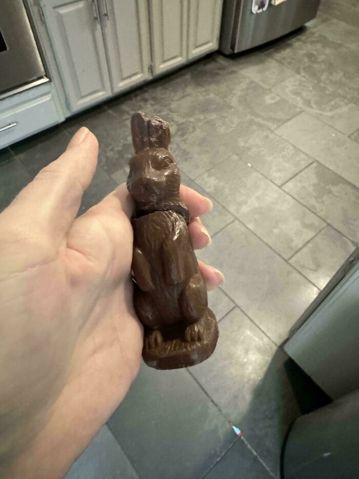 Hand holding a damaged chocolate bunny in a kitchen, an unfortunate event that might lighten your day.