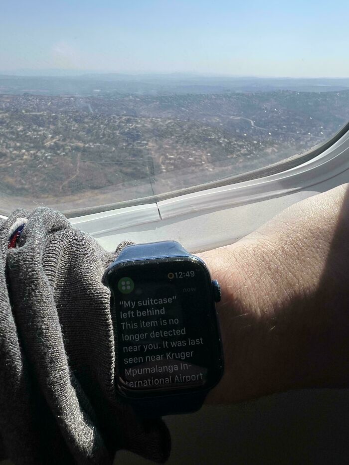 Smartwatch alert about lost suitcase seen near airplane window, capturing an unfortunate event from traveler’s perspective.
