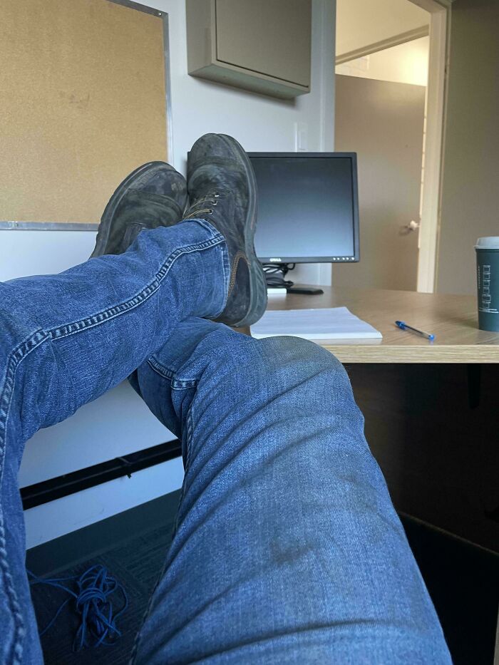 Person wearing dirty boots and jeans resting feet on an office desk in a photo of unfortunate events