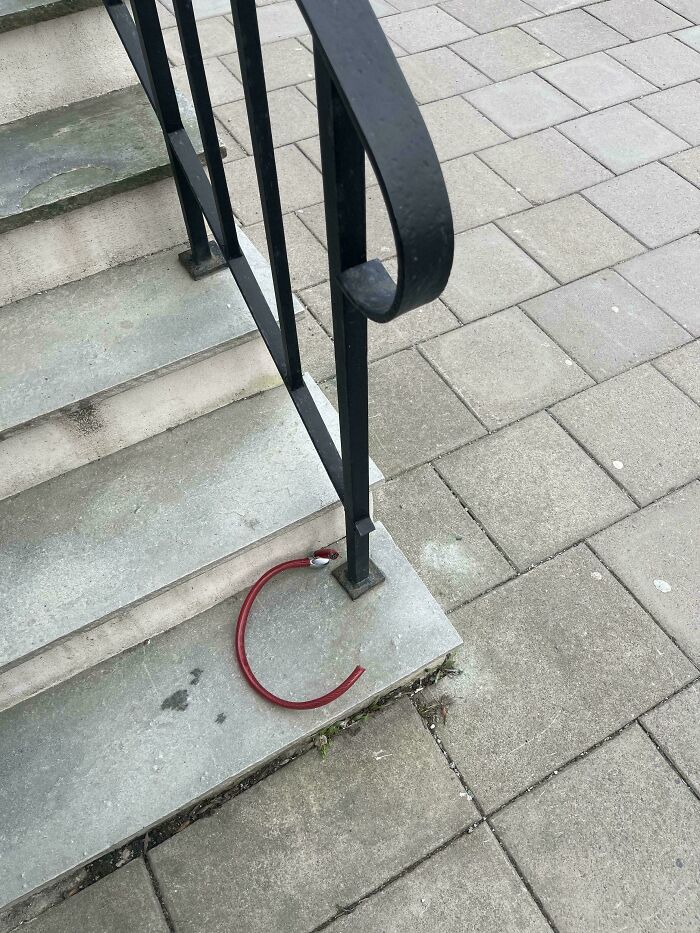 A broken red bike lock left on outdoor stairs railing, illustrating unfortunate events that make you feel better about your day.